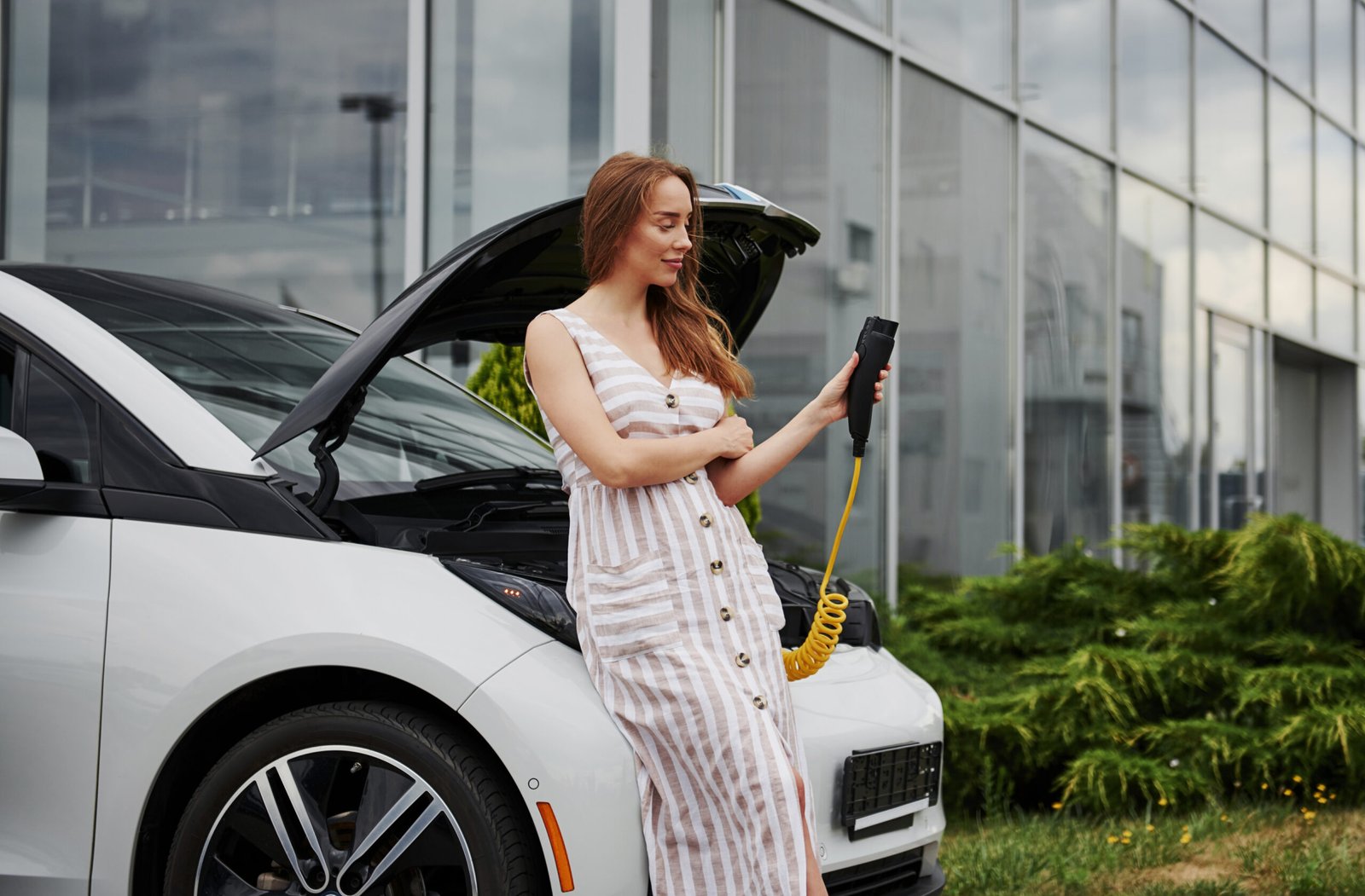 Femme consultant un appareil pendant la recharge d'une voiture électrique Femme consultant un appareil pendant la recharge d'une voiture électrique
